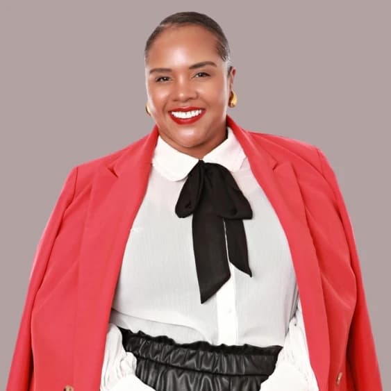 Erika, a confident and professional team member, wearing a red blazer over a white blouse with a black bow tie, smiling warmly