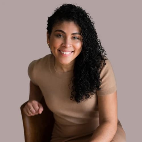 Taissha, wearing a beige dress, smiling warmly while seated